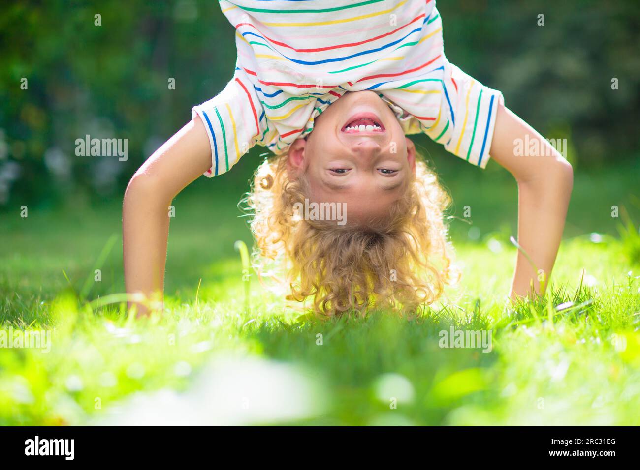 Der kleine Junge hängt kopfüber. Handstand-Übungen für kleine Kinder. Aktives Kind spielt auf sonnigen Gartenrasen. Sommerspaß. Kinder spielen draußen. Stockfoto