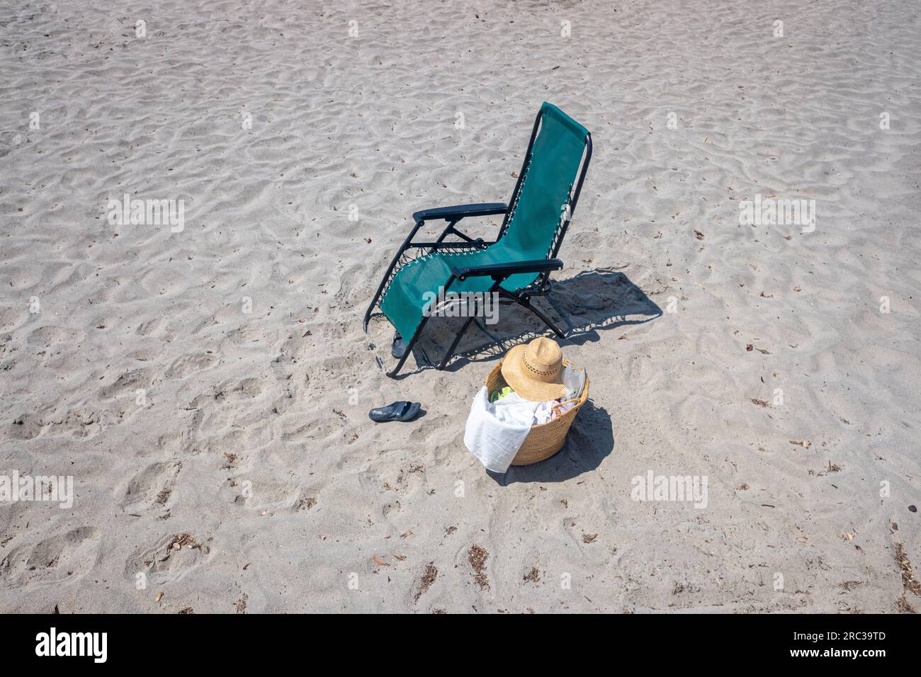 Abgeschiedene Liege am Strand, Sandalen und ein Korb mit Strandartikeln und einem Hut Stockfoto
