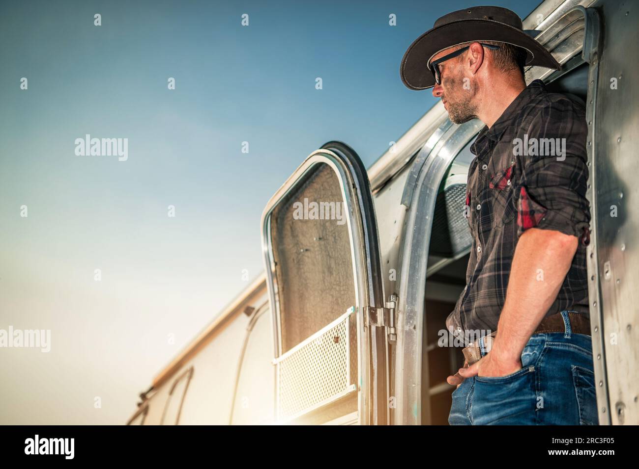 Entspannter weißer Cowboy in seinem 40s und seinem Classic Shiny Travel Trailer. Amerikanisches West-Thema. Stockfoto