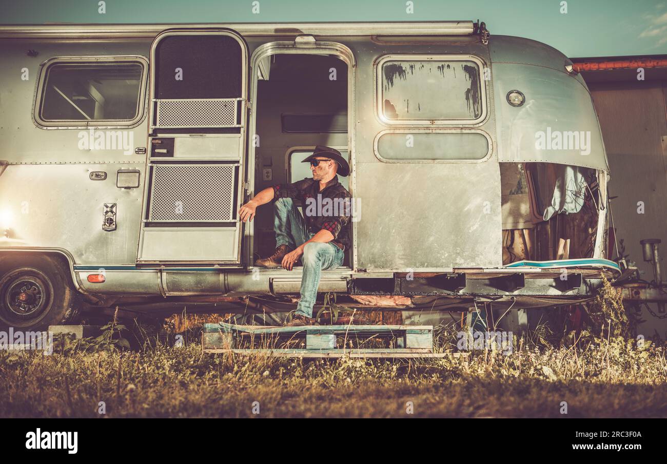 Der kaukasische amerikanische West Cowboy entspannte sich in seinem 40s-Sitzer in seinem Vintage Travel Trailer. Projekt Zur Wiederherstellung Von Anhängern Stockfoto
