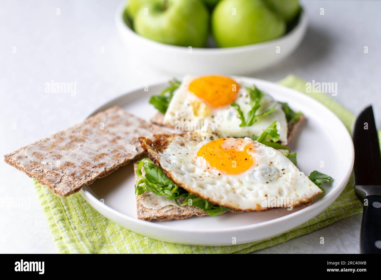 Glutenfreier und vegetarischer Frühstücksteller mit kohlenhydratarmem Cripbread, Rucola, Spiegeleiern und grünen Äpfeln auf weißem Hintergrund Stockfoto