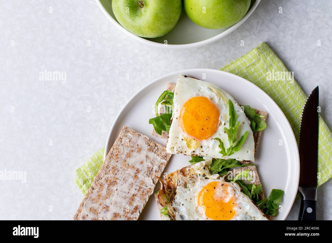 Gesundes Frühstück mit Spiegeleiern, Rucola, Knäckebrot und grünem Apfel auf hellem Hintergrund Stockfoto
