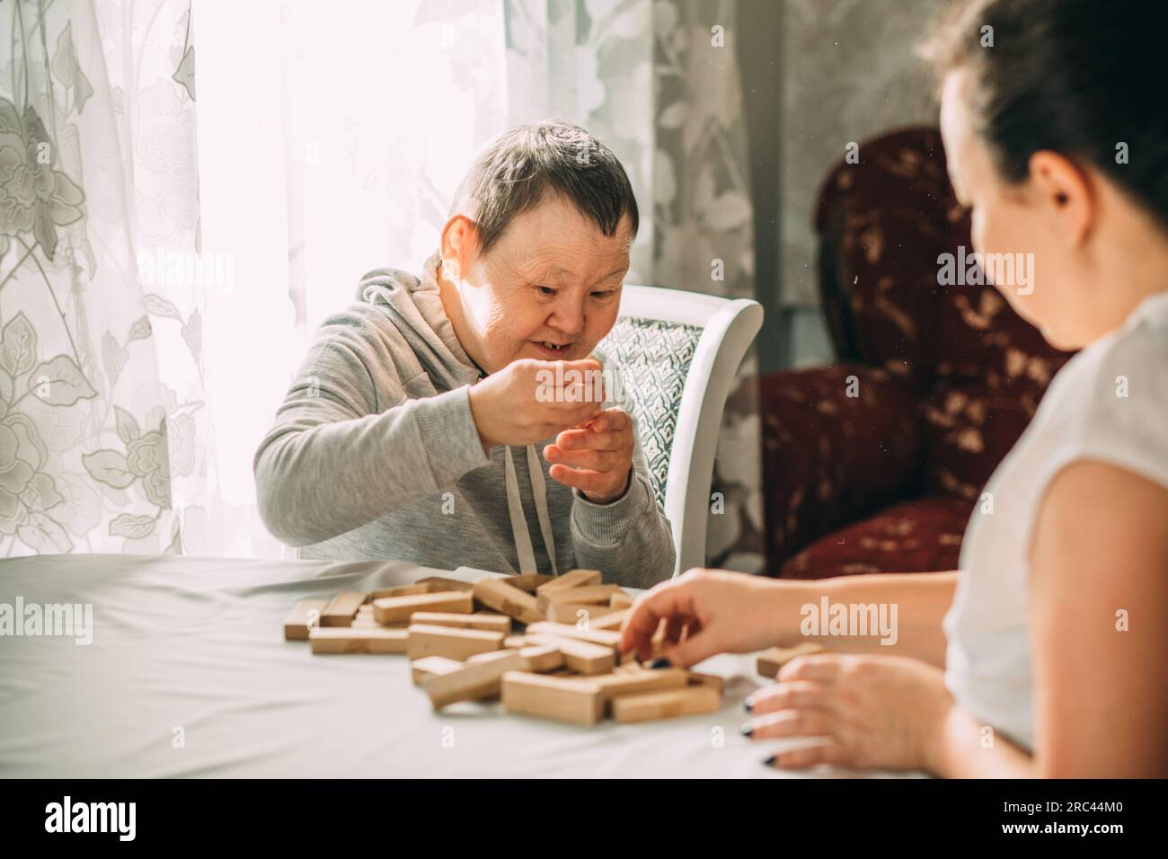 Ältere Frau mit Down-Syndrom baut einen Turm aus Holzblöcken, Bildungsprogramm, Arbeit mit einem Lehrer Stockfoto