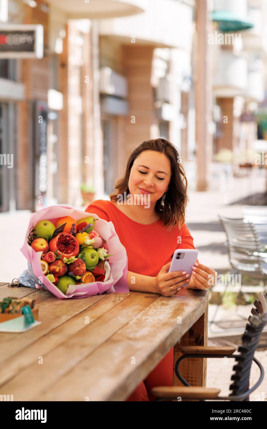 Eine schöne Geschäftsfrau in einem roten Kleid arbeitet und bewundert das Geschenk eines essbaren Blumenstraußes Stockfoto
