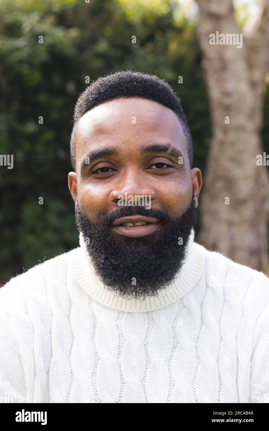 Porträt eines glücklichen afroamerikanischen Mannes mit kurzen Haaren, der im Garten einen weißen Pullover trägt Stockfoto