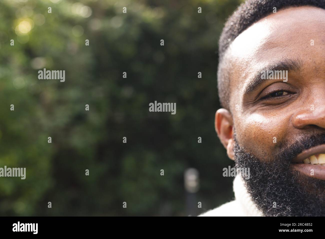 Porträt eines glücklichen afroamerikanischen Mannes mit kurzen Haaren, der im Garten einen weißen Pullover trägt Stockfoto