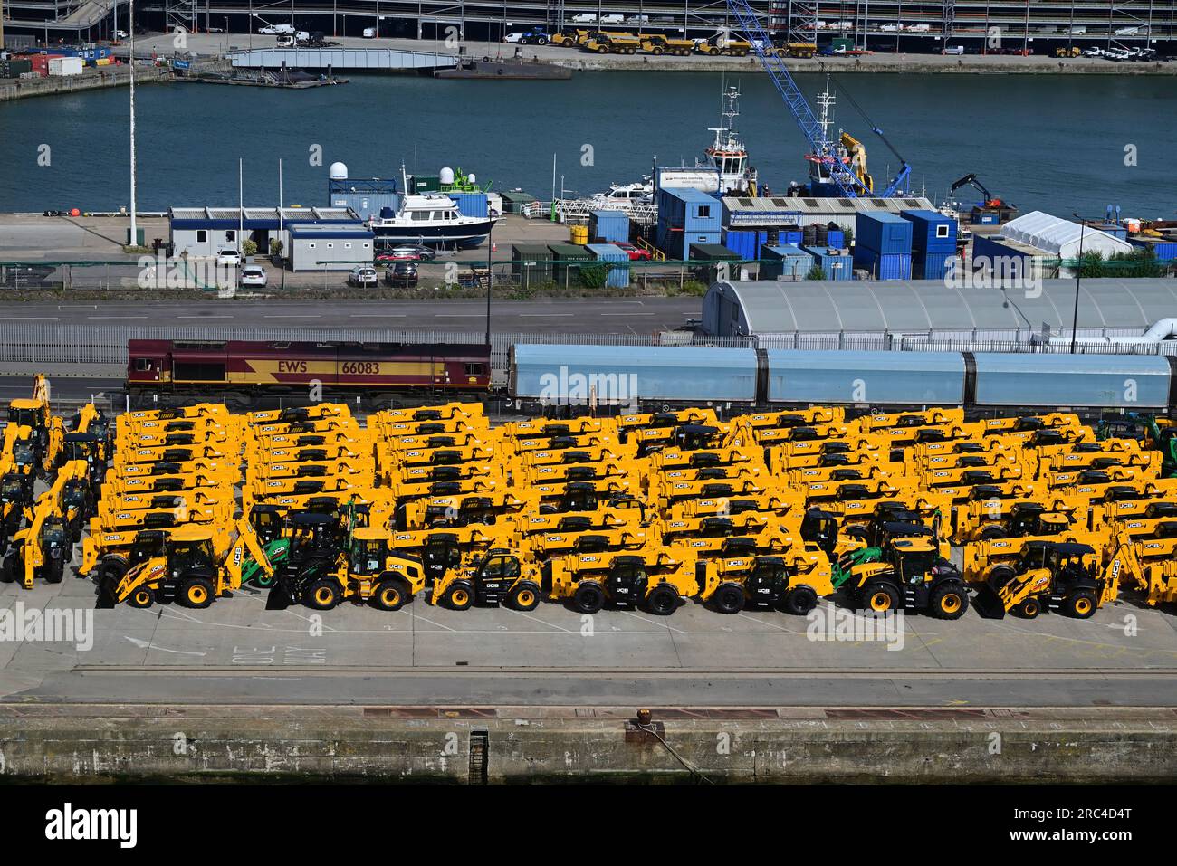 EWS Klasse 66 dieselelektrische Güterlokomotive Nr. 66083, die einen Autoträgerzug an den Southampton Docks steuert, mit gelben JCB's am Kai. Stockfoto