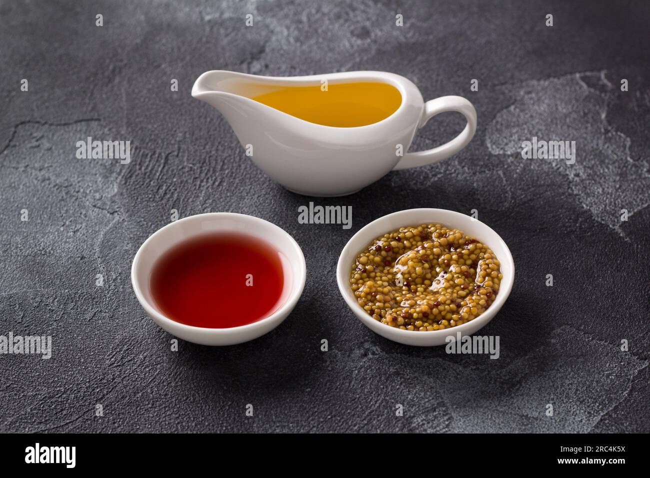 Weinessig, Senf, Pflanzenöl auf dunklem, strukturiertem Hintergrund. Inhaltsstoffe Der Vinaigrette-Sauce. Stockfoto