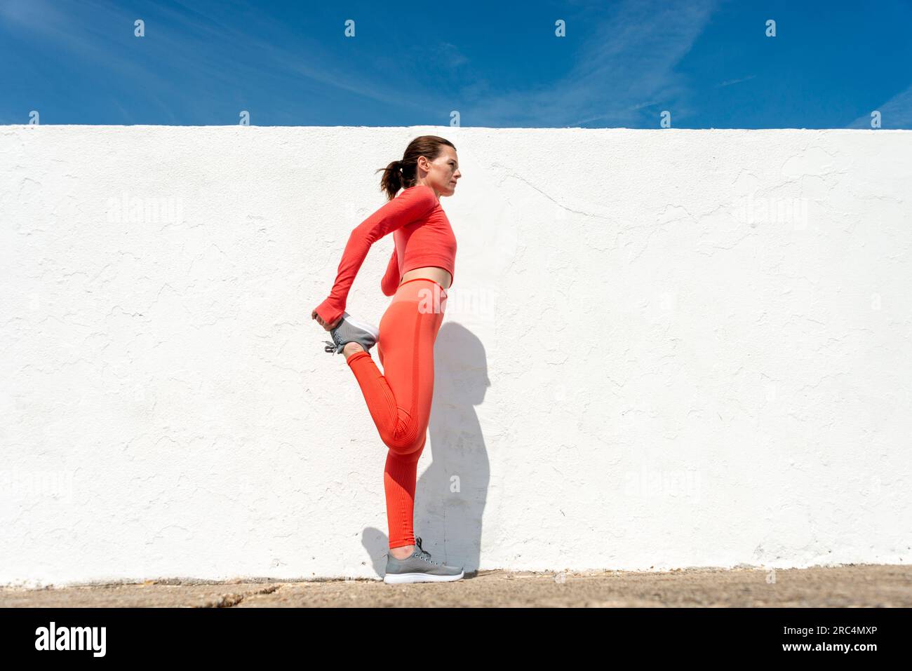 Sportliche Frau, die im Freien in der Sonne Beindehnungsübungen macht Stockfoto
