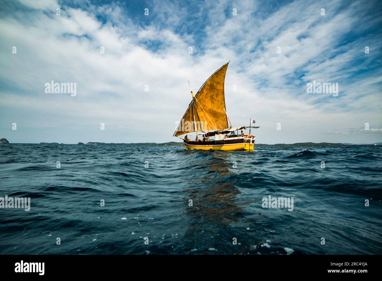 Fischerboot, das auf rauschenden Meerwasser mit offenem gelbem Segel an Deck mit Seilen gefesselt ist, während es an einem sonnigen Tag vor blauem, wolkigen Himmel festgemacht ist Stockfoto