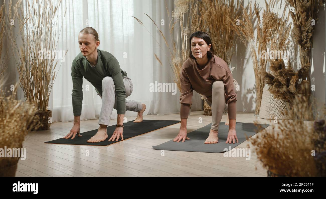 Der ganze Körper eines erwachsenen Barfußpaares mit geschlossenen Augen macht einen Ausfallschritt auf der Matte, während der vordere Fuß das Körpergewicht trägt und die Hände auf dem Boden Yoga üben Stockfoto