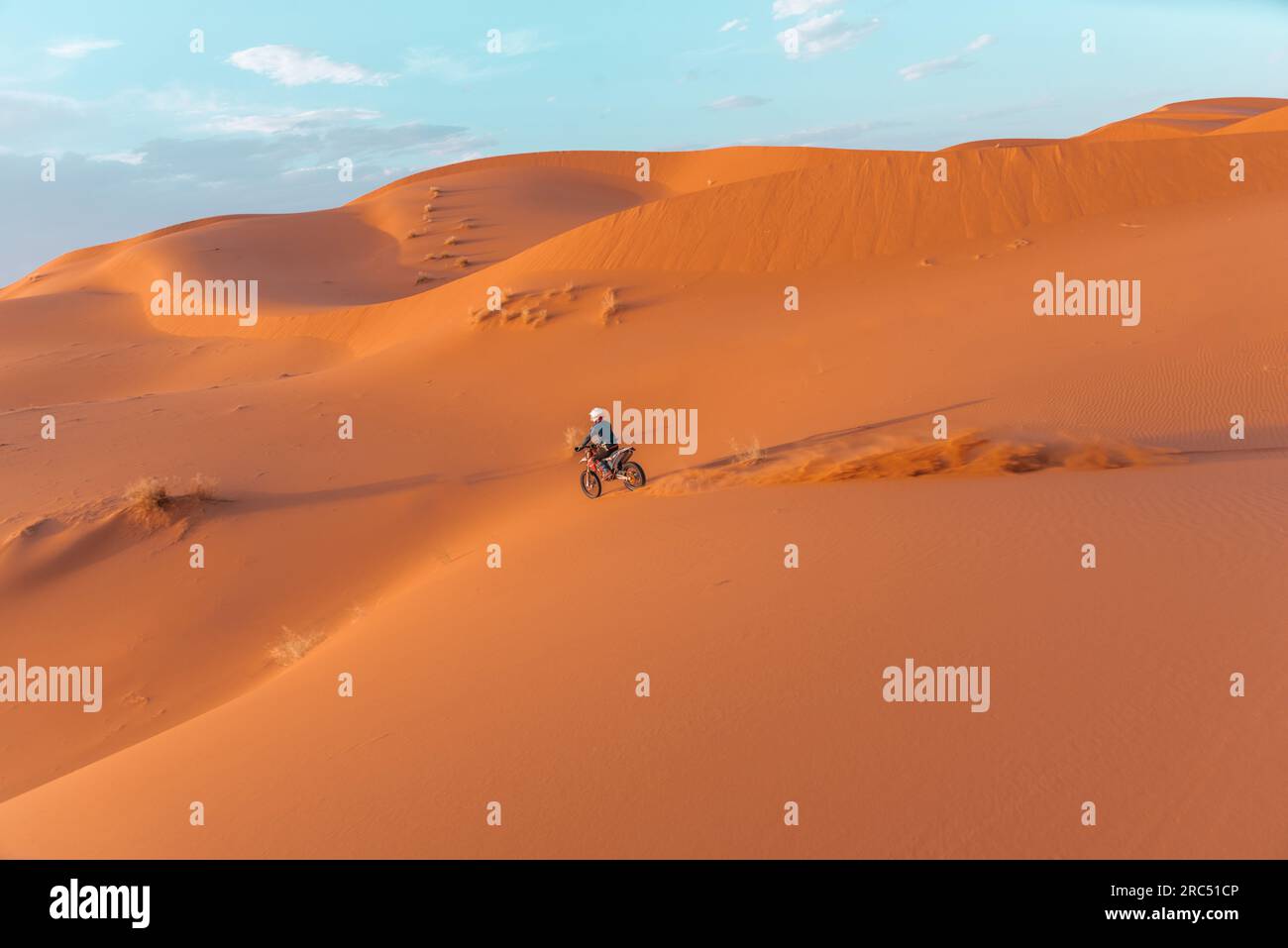 Seitenansicht einer nicht wiedererkennbaren Person, die Motorrad auf Sanddünen vor bewölktem Himmel in der Merzouga-Wüste Marokko fährt Stockfoto