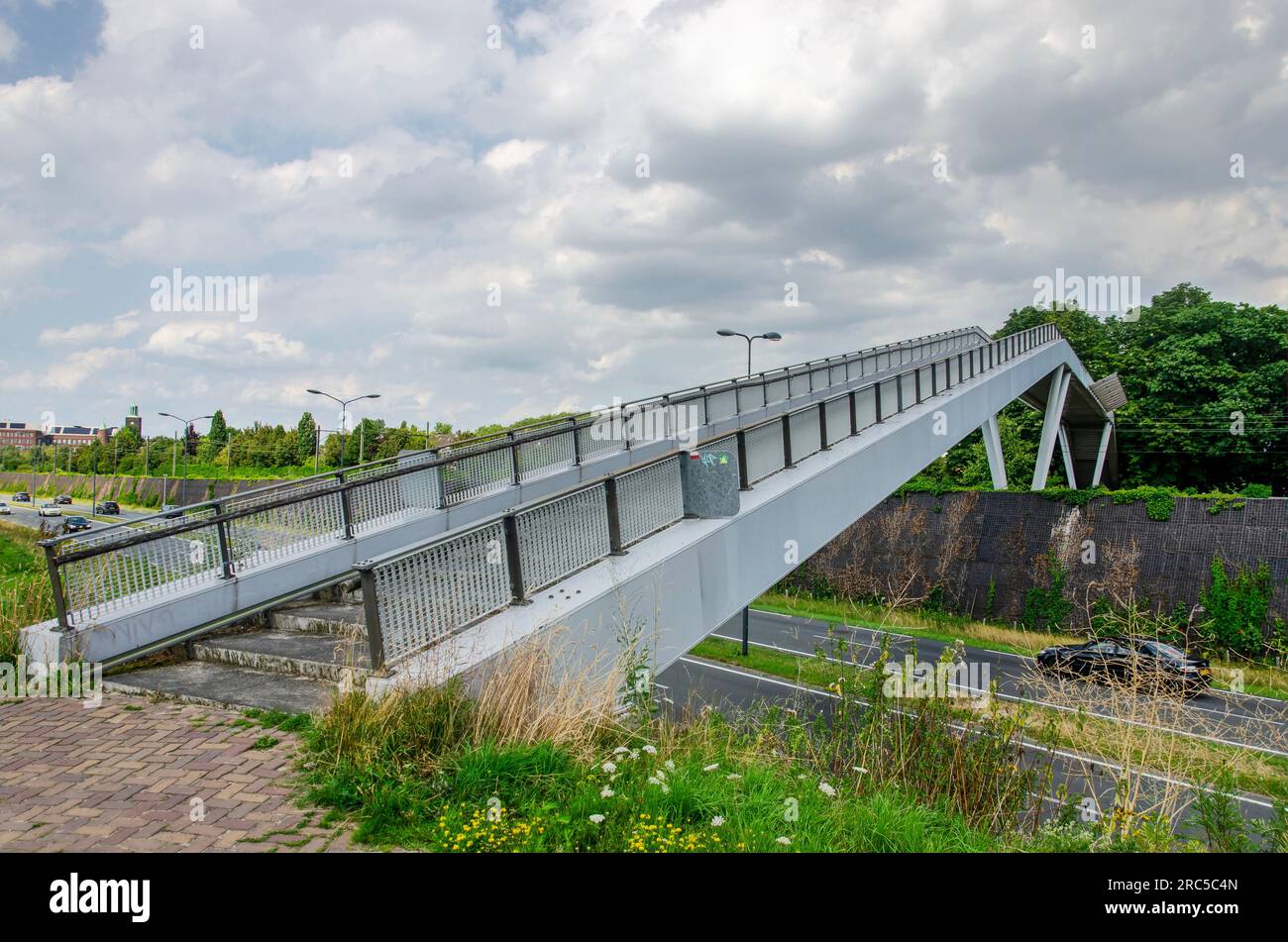 Vught, Niederlande, 10. Juli 2023: Fußgängerbrücke aus Stahl, die sowohl eine verkehrsreiche Straße als auch eine Eisenbahnstrecke überquert Stockfoto
