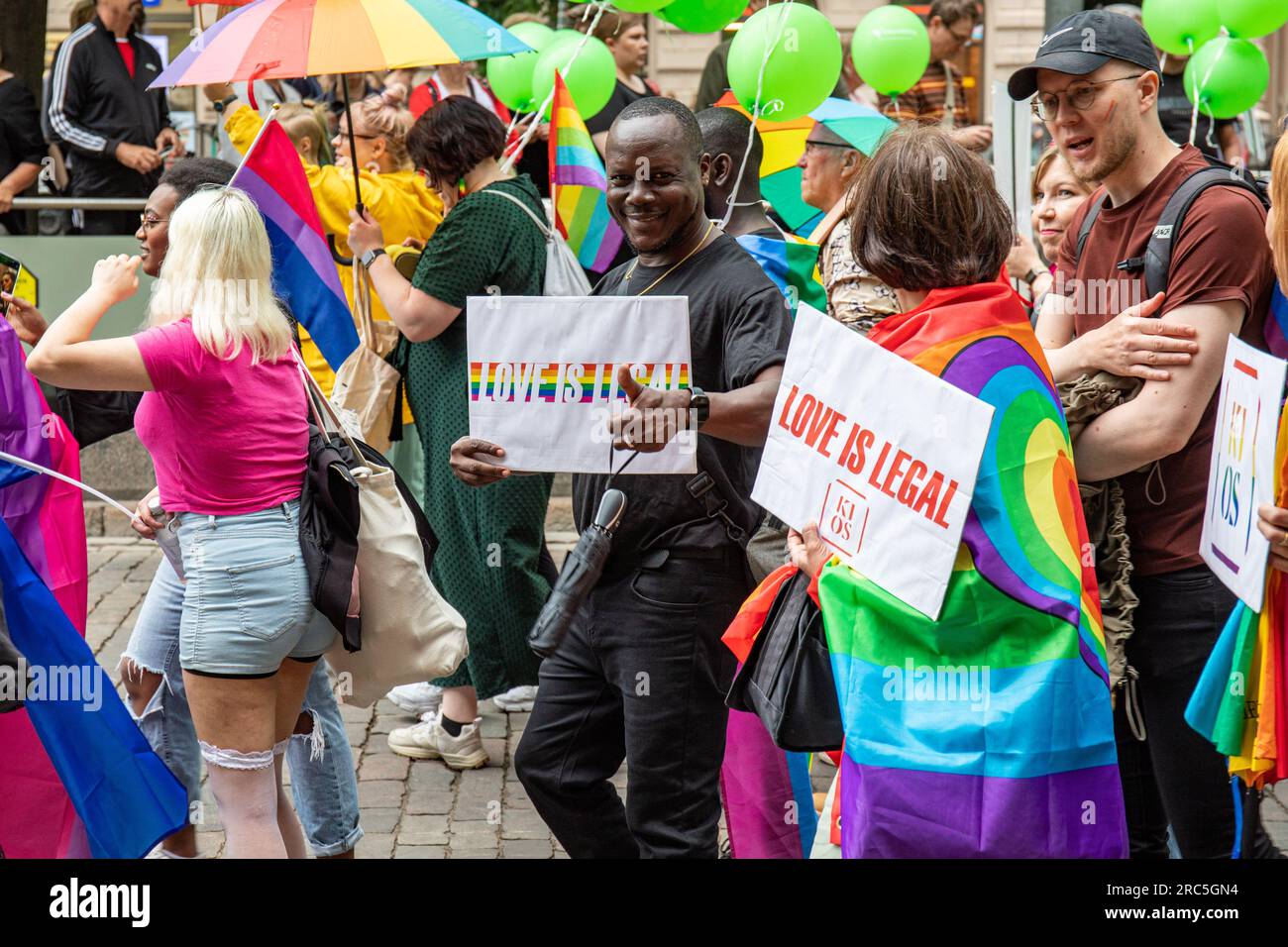 Liebe ist legal. Personen mit gedruckten Schildern mit KIOS-Logo auf der Helsinki Pride 2023 Parade in Helsinki, Finnland. Stockfoto