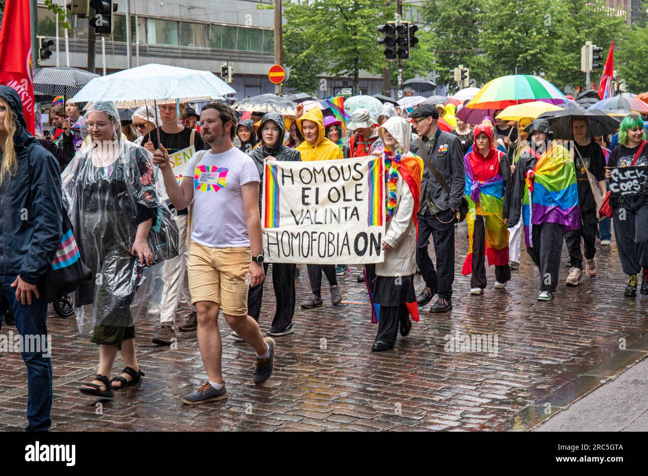 Teilnehmer tragen Banner und Regenschirme bei der Helsinki Pride 2023 Parade an einem Regentag in Helsinki, Finnland Stockfoto