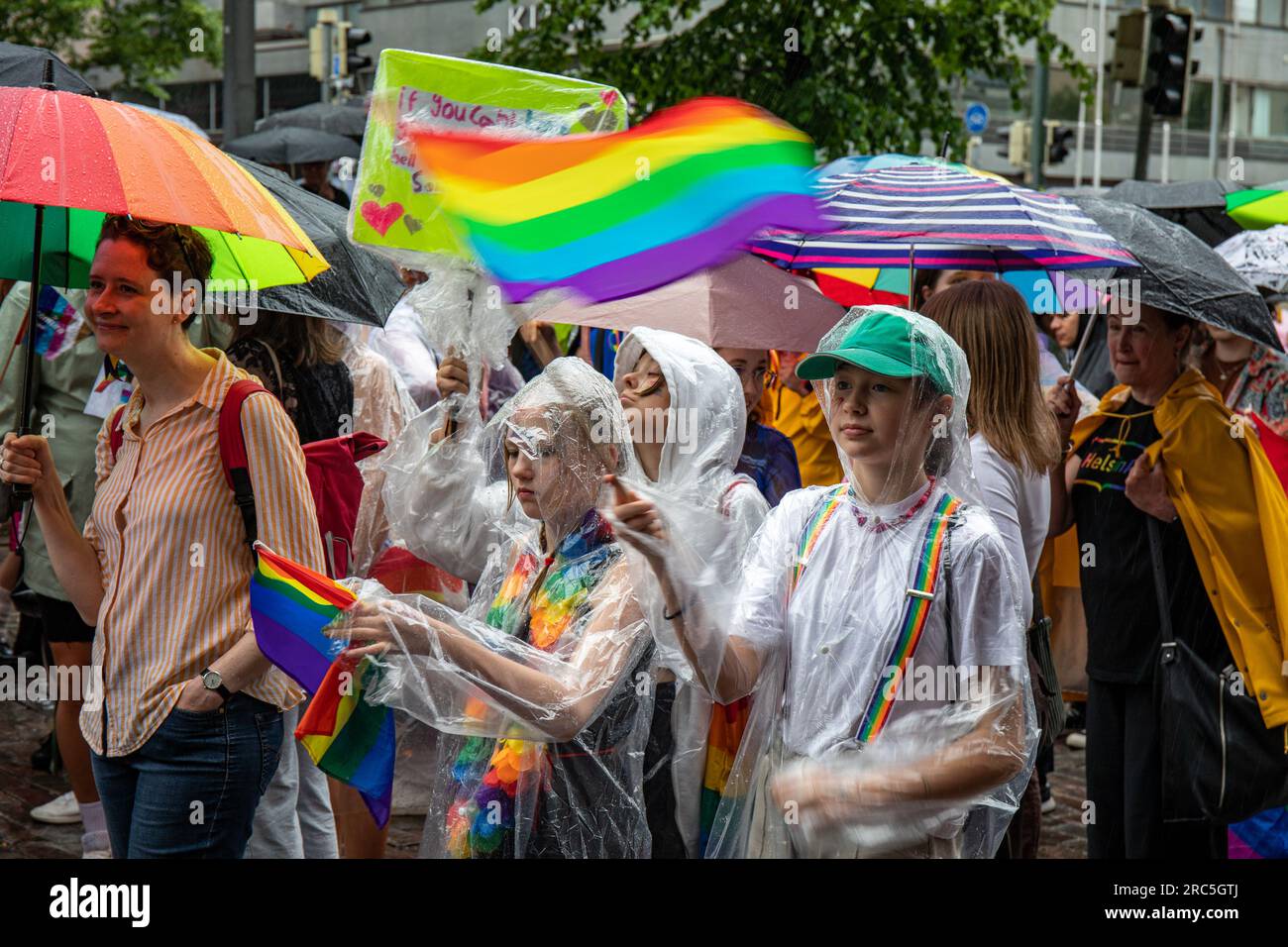 Junger Teilnehmer, der bei der Helsinki Pride 2023 Parade an einem Regentag in Helsinki, Finnland, mit einer stolzen Flagge wedelt Stockfoto
