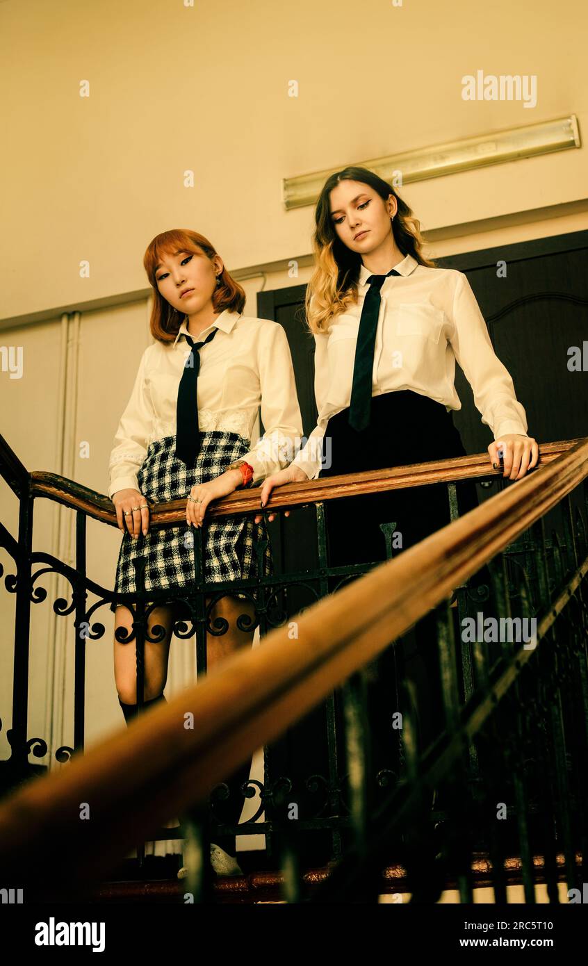 Auf der Schultreppe sehen zwei hübsche Schulmädchen in Uniformen mit einem traurigen Ausdruck nach unten. Melancholie, Introspektion und die Stru Stockfoto