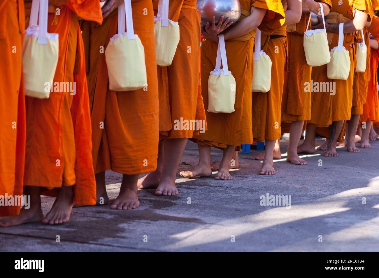 Füße orangefarbener theravada buddhistischer Mönche, die in Thailand Almosen suchen. Stockfoto