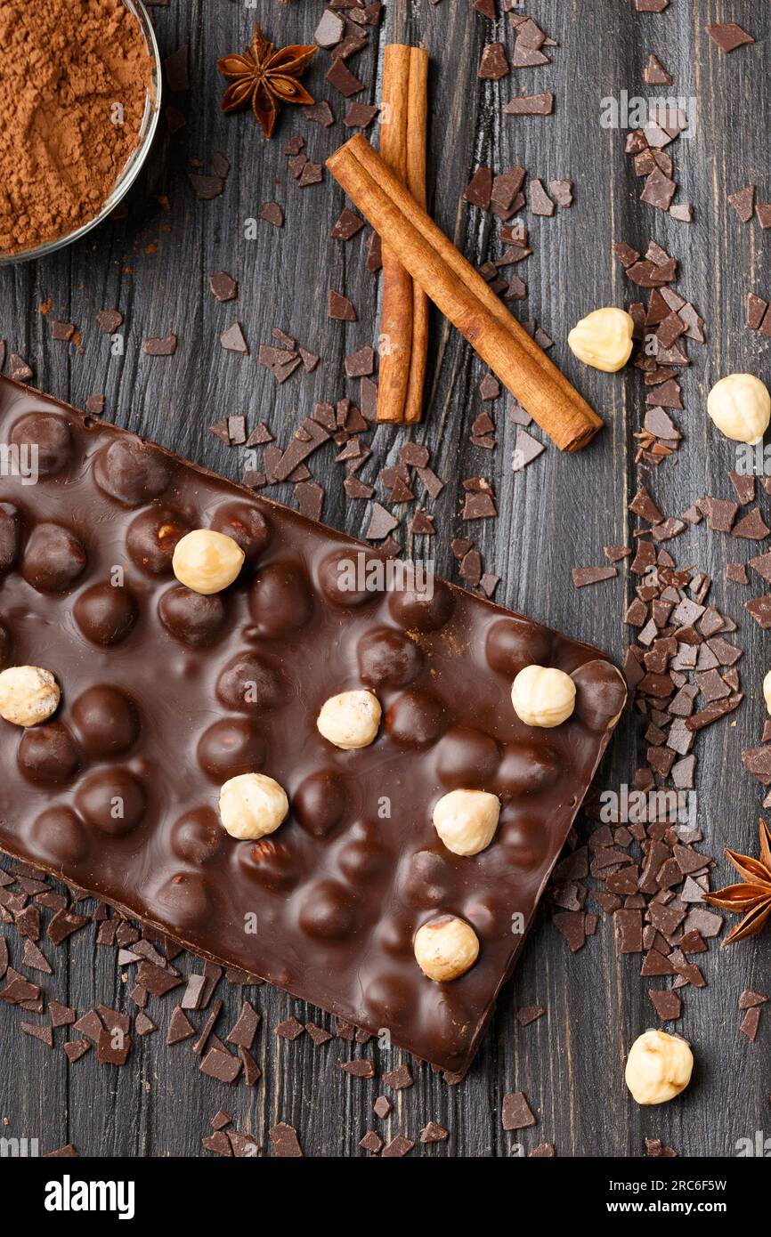 Handgemachte Schokolade mit Haselnüssen, dunklen Schokoladenstücken, Kakao auf dunklem Holzhintergrund mit Blick von oben. Schokoladenvariante. Stockfoto