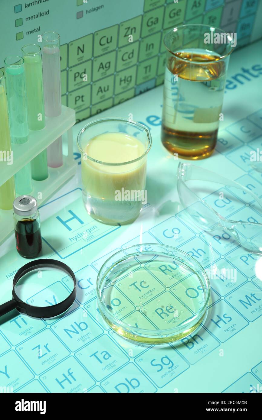 Verschiedene Laborgeräte mit Flüssigkeiten und Schutzbrillen auf dem Periodensystem chemischer Elemente. Hellgrüner Toneffekt Stockfoto