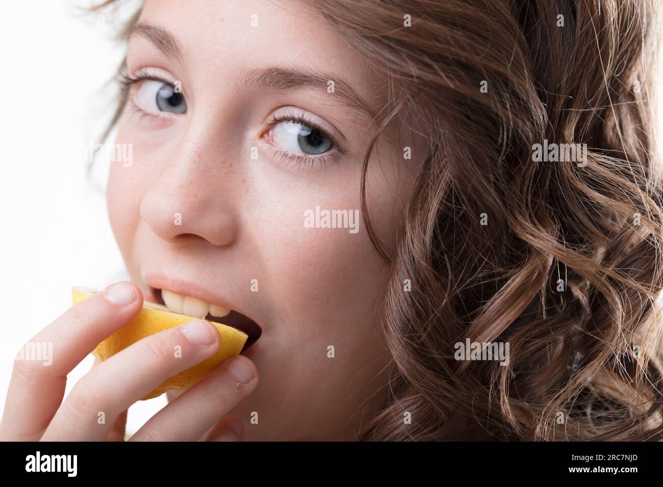 Ein Mädchen mit Locken beißt in eine Zitrone, erfährt seine pikante Vitalität, symbolisch für die Gesundheit Stockfoto