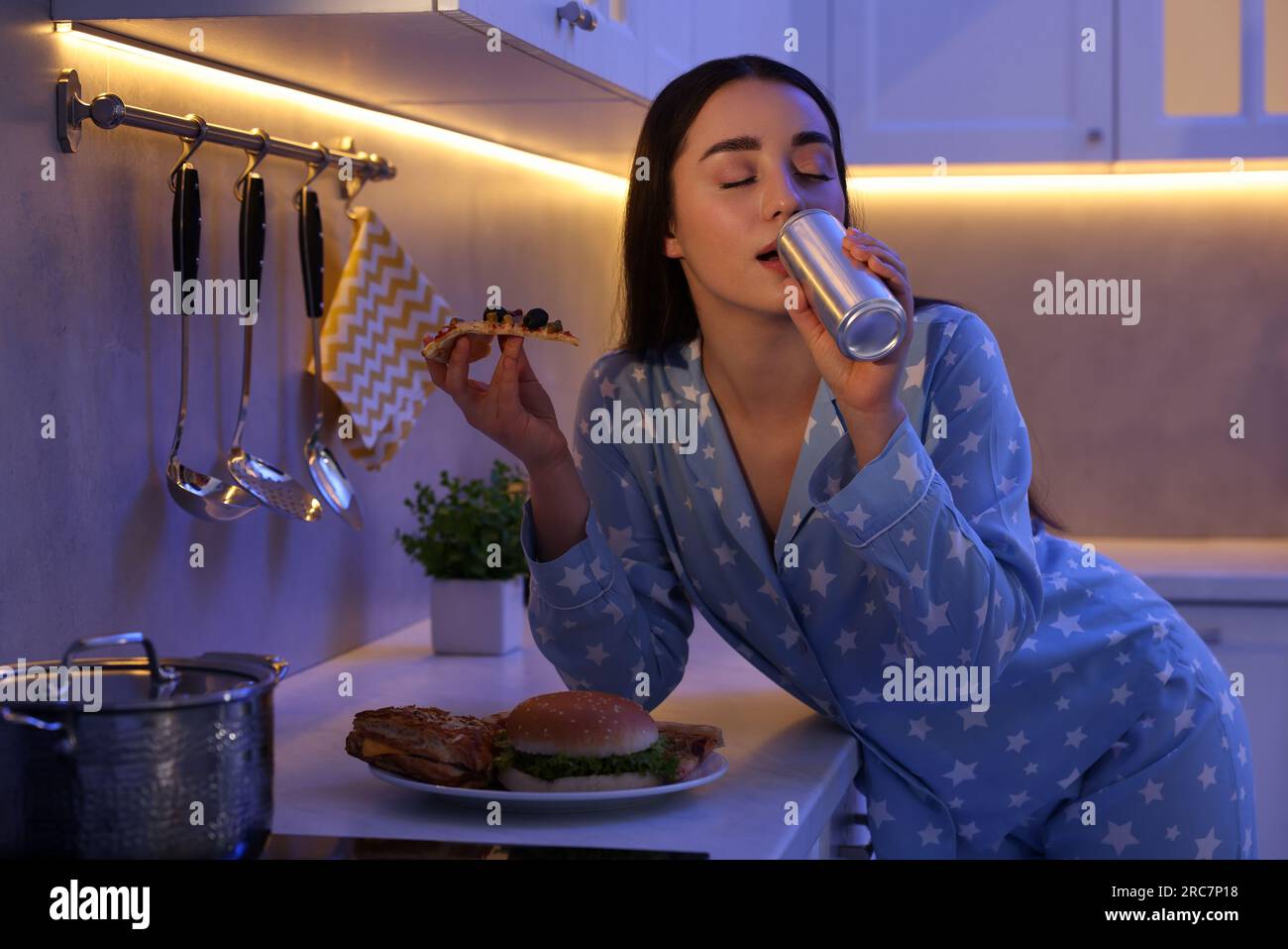 Junge Frau, die abends Junkfood in der Küche isst. Schlechte Angewohnheit Stockfoto