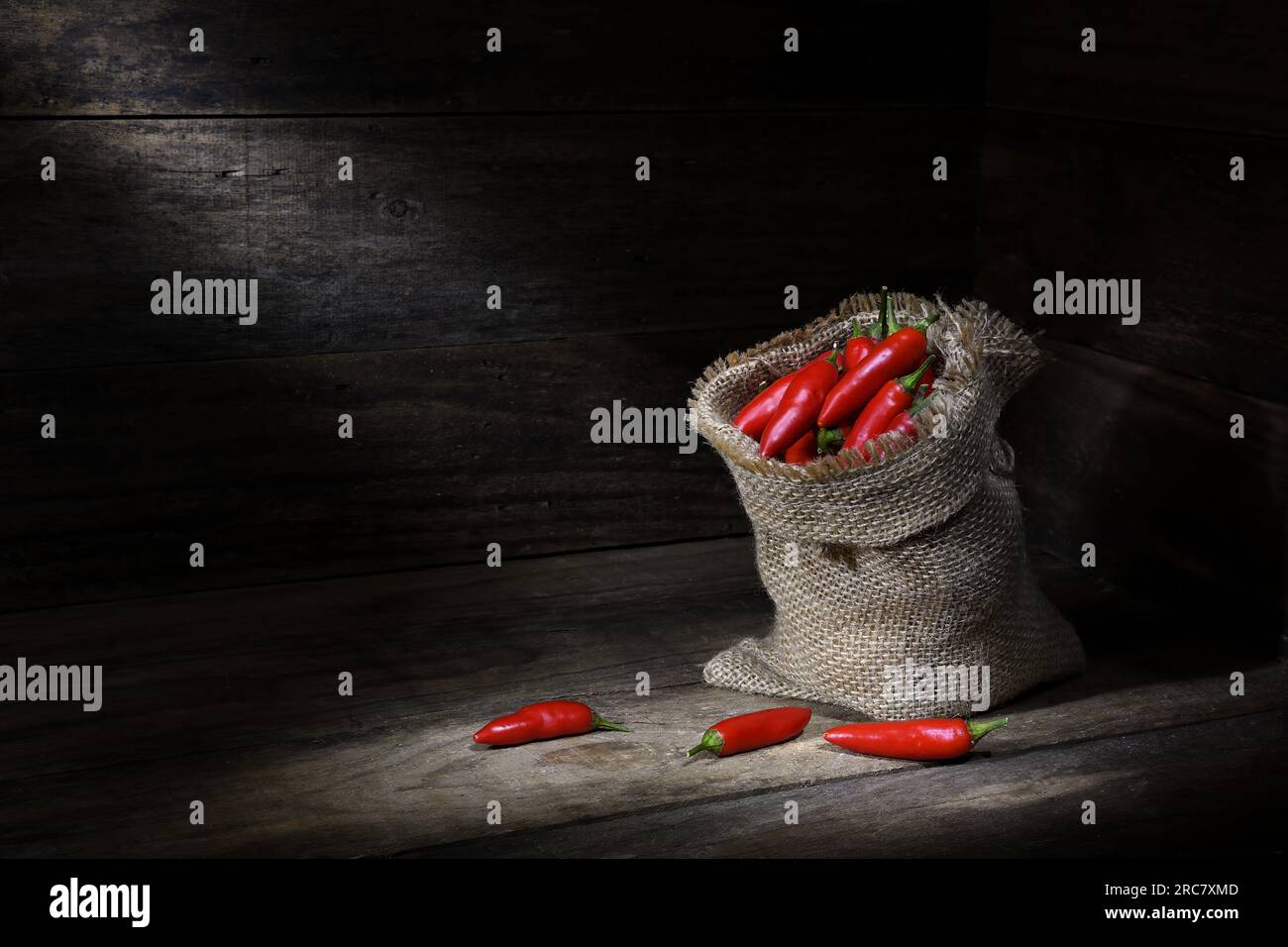 Ein Stilleben einer hessischen Tasche voller roter Chili-Paprika in einer rustikalen Holzbox mit Pools mit sanfter dunkler Stimmungsbeleuchtung und Kopierbereich Stockfoto