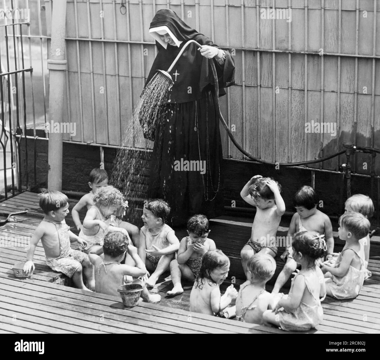 New York, New York: 1. Juli 1941 Es ist ein heißer Tag in New York City und eine Schwester kühlt ein paar ihrer Kinder in der Kindertagesstätte Madonna House Day Nursery ab. Stockfoto