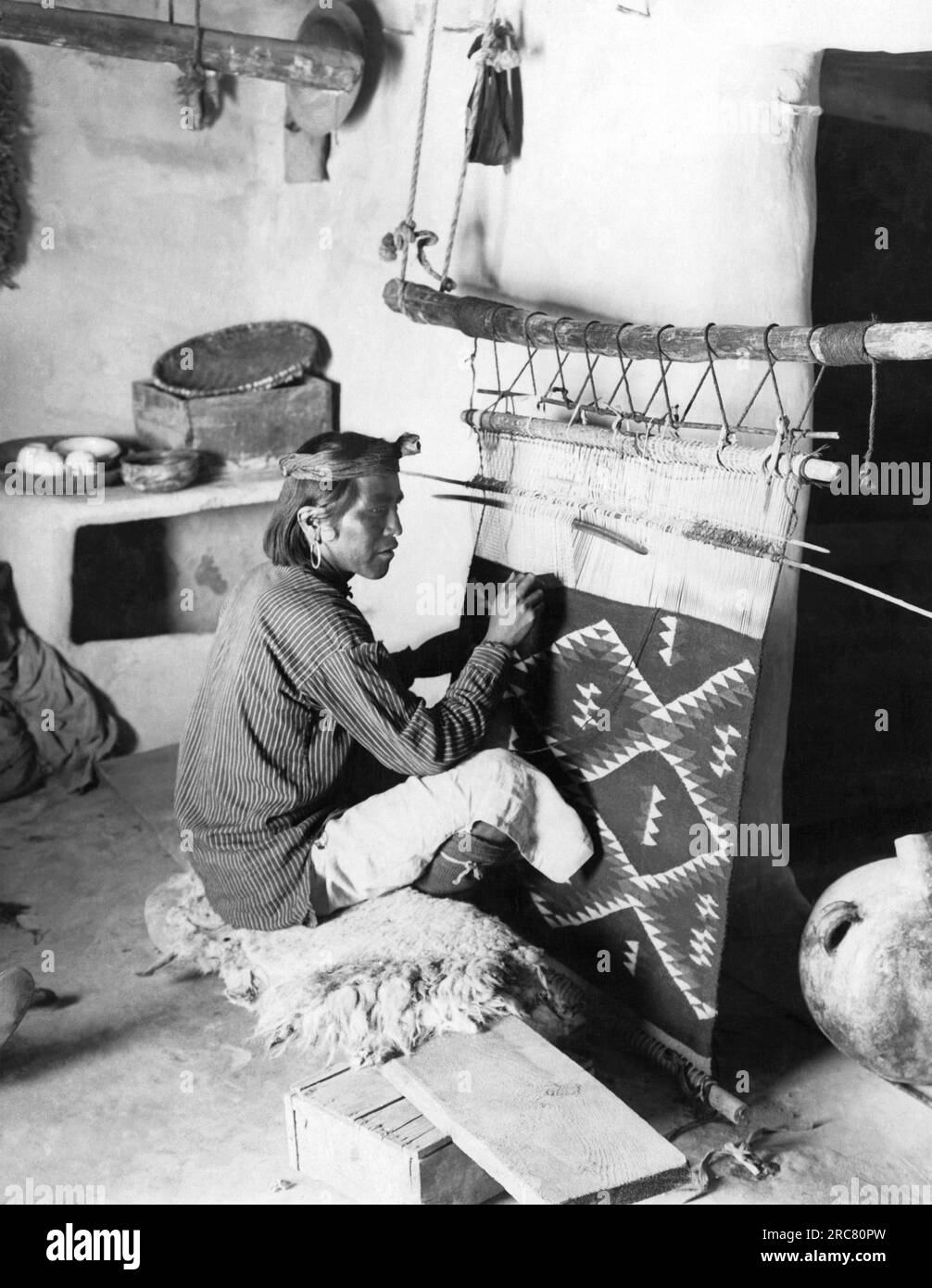 Amerikanischer Südwesten: ca. 1920 Ein Navajo-Mann sitzt an seinem Webstuhl und webt eine Decke. Stockfoto