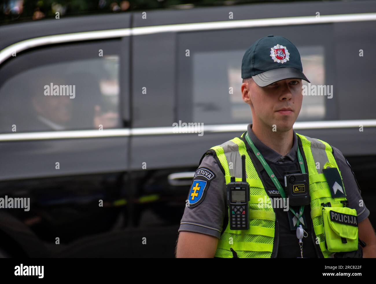 Litauischer Sicherheitspolizist mit US-Präsident Joe Biden, der während des NATO-Gipfels 2023 im Zentrum von Vilnius im Auto im Hintergrund verzichtete Stockfoto