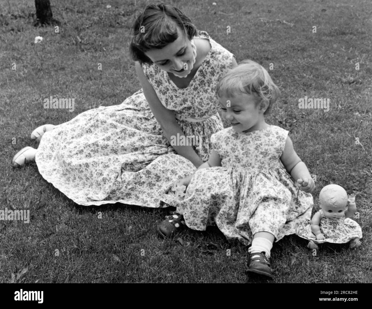 Illinois: ca. 1955 Eine Mutter und ihre Tochter mit ihrer Puppe auf einem Rasen in passenden Outfits. Stockfoto
