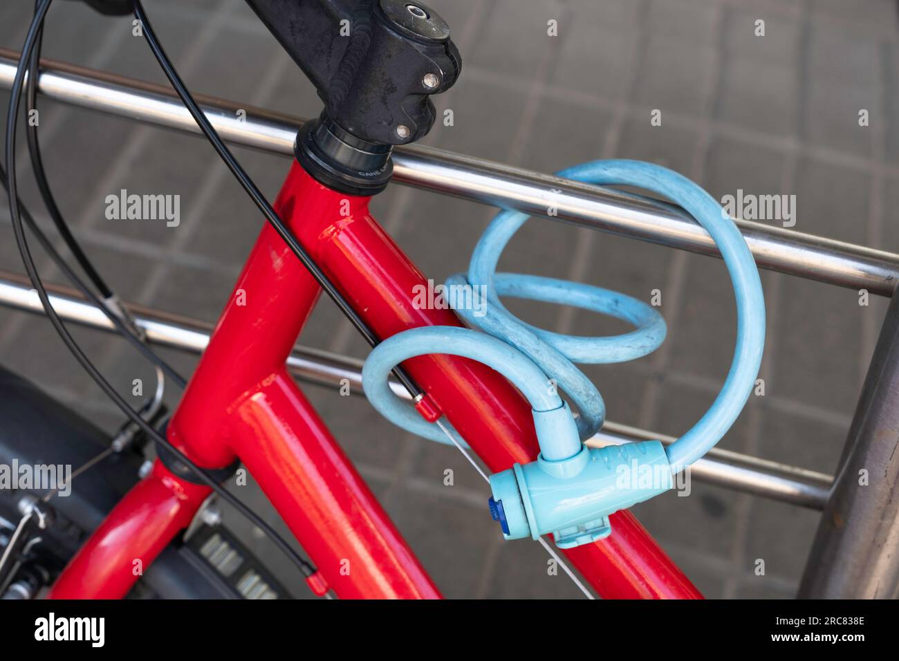 Das rote Fahrrad ist mit einem blauen Fahrradkabelschloss sicher an einem Edelstahlrohr befestigt. Detail Stockfoto