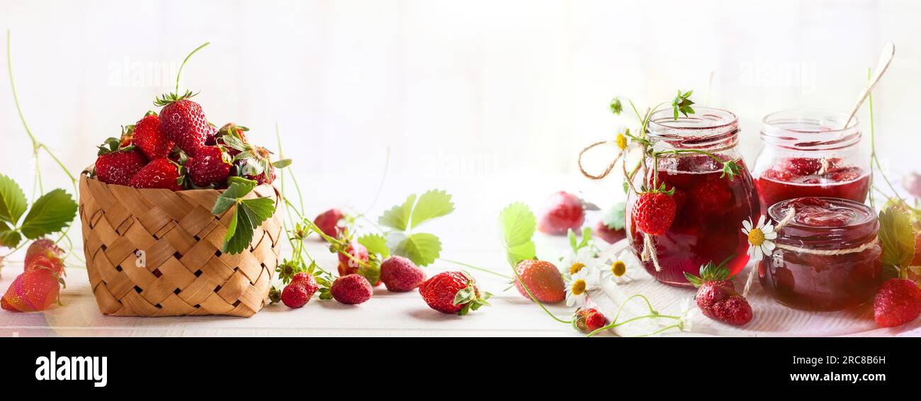 Erdbeeren hausgemachte Marmelade in Glasgefäßen und frische Beeren im Korb mit Sommerblumen auf Holztisch im rustikalen Stil Stockfoto