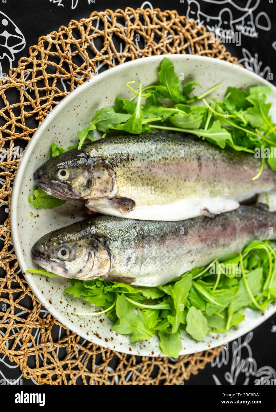 Zwei rohe Forellen auf einem Teller, garniert mit vielen frischen grünen Blättern, Nahaufnahme. Zubereitung der Mahlzeiten. Stockfoto