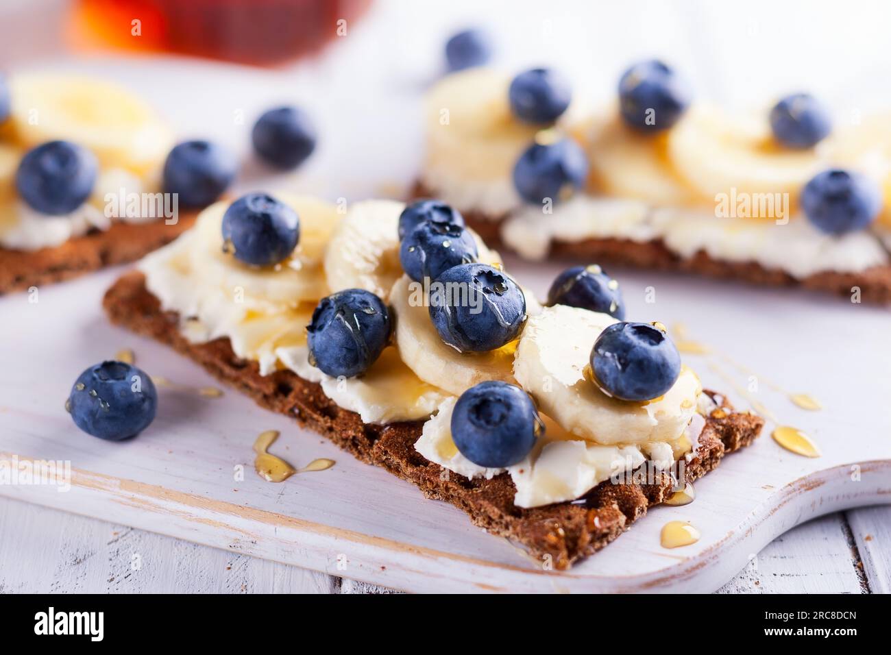 Gesunde Sandwiches mit Beeren, Obst, Honig und Frischkäse auf weißem Holzschwein Stockfoto