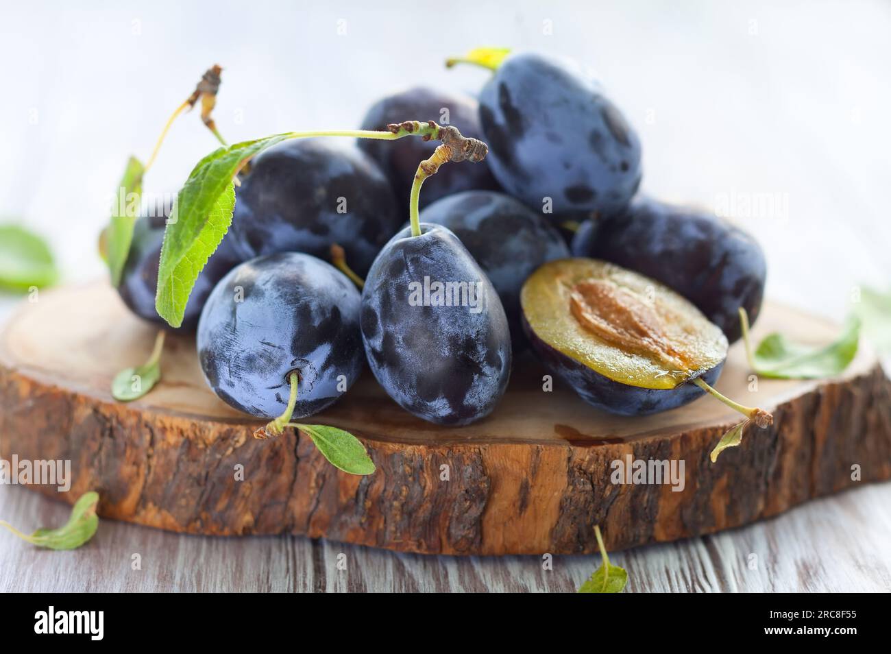 Frische Pflaumen mit Blättern auf Holzhintergrund Stockfoto