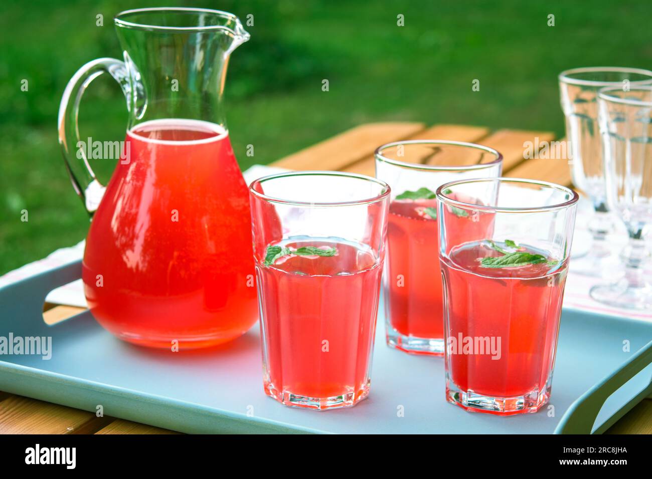 Himbeersaft in einer Kanne und Gläser im Garten. Sommergetränk für heiße Tage. Roter Fruchtsaft im Freien. Stockfoto