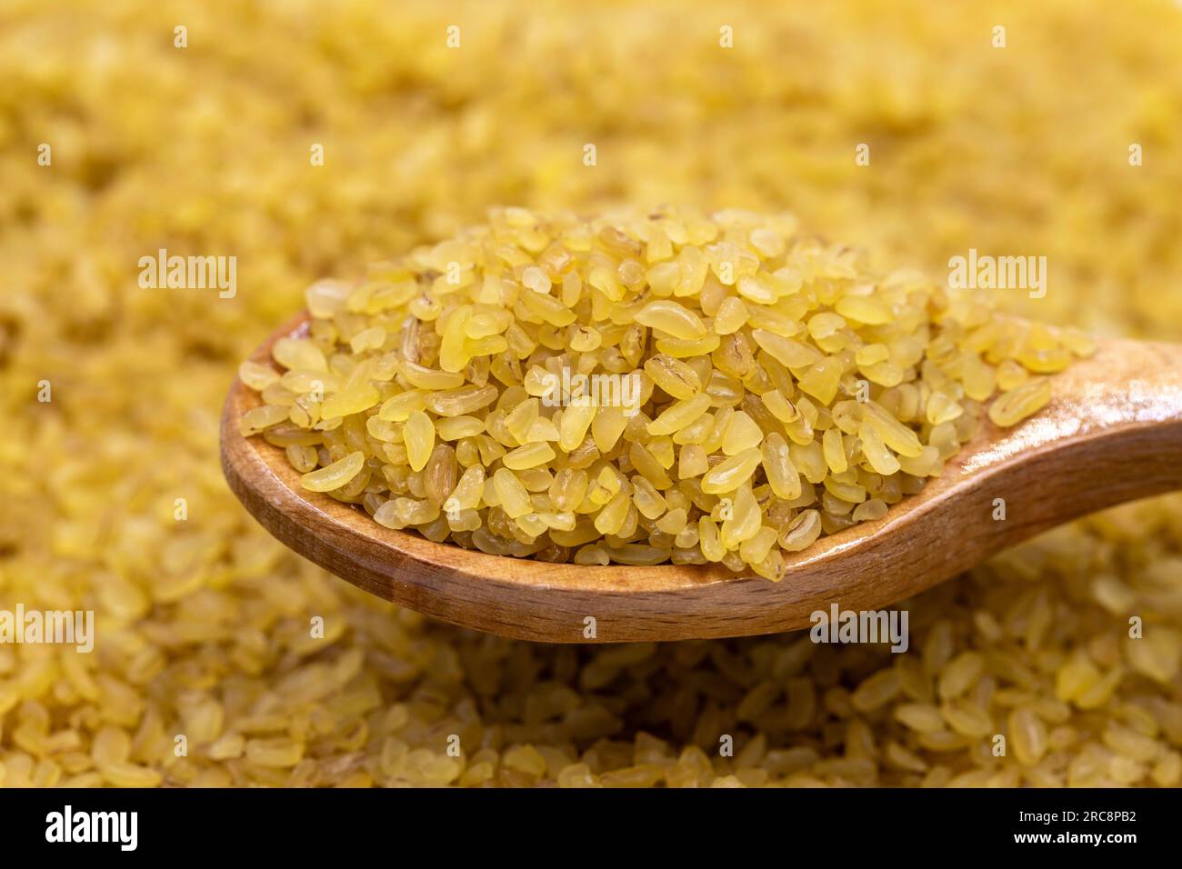 Rohbulgur-Weizen auf Holzlöffel, Hülsenfrüchte als Hintergrund. Nahaufnahme von ungekochtem trockenem Bulgur-Weizen Stockfoto