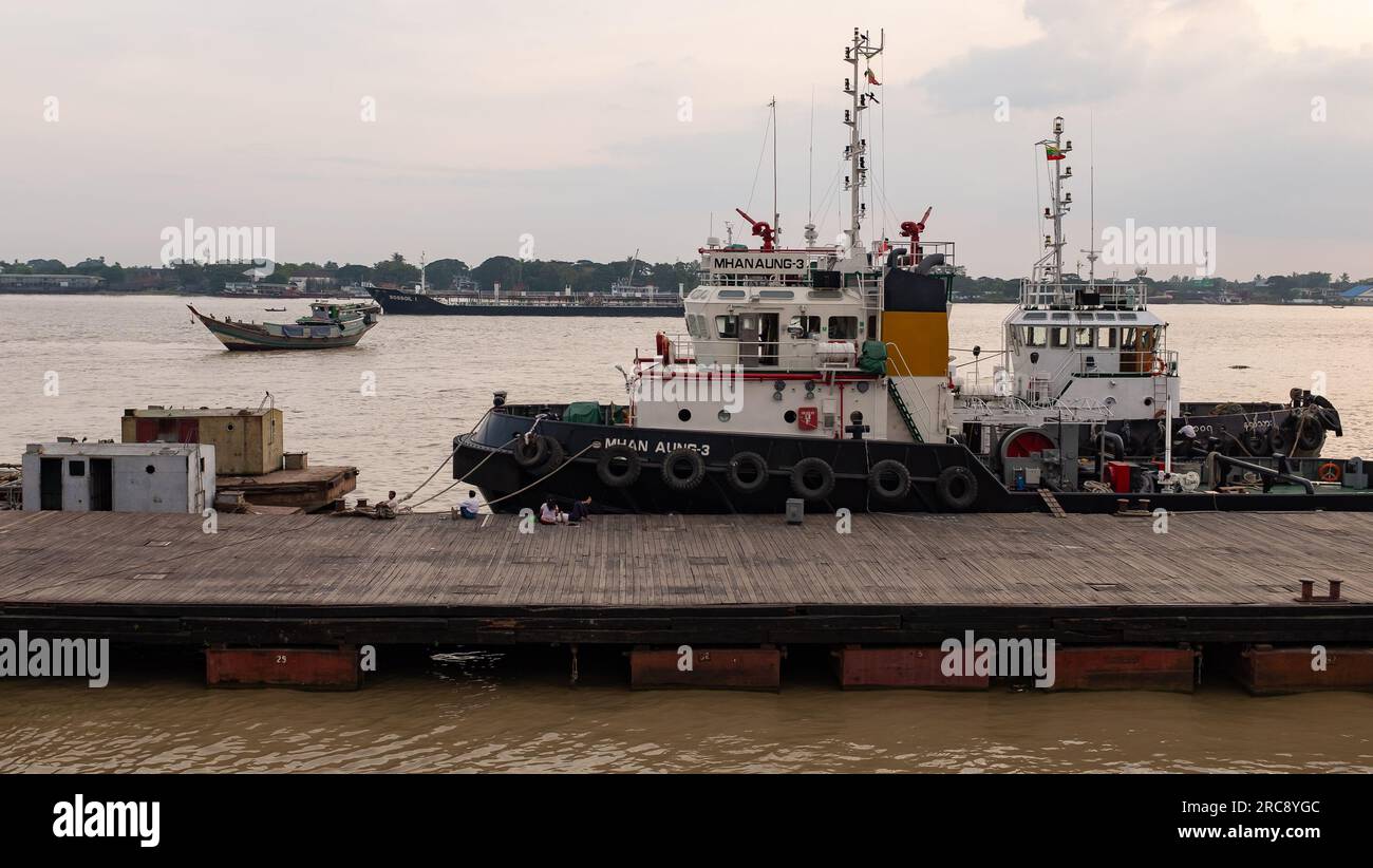 Yangon, Myanmar, 2014. Die Leute sitzen auf dem Steg und beobachten die Boote auf dem Rangoon River vor Sonnenuntergang Stockfoto