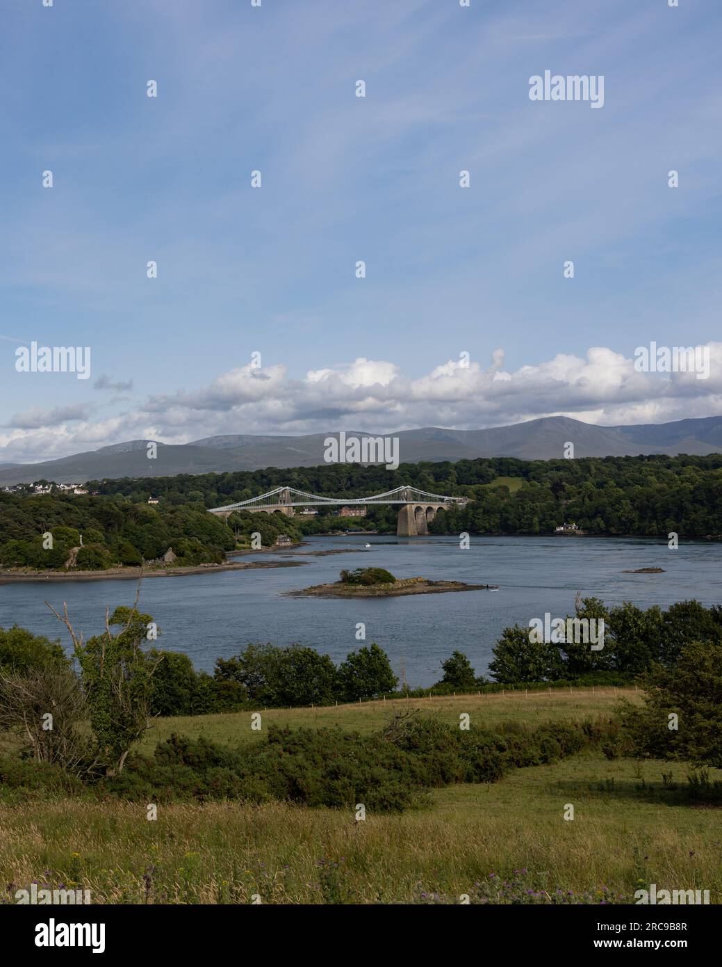 Die Menai-Straße trennt Anglesey vom Rest von Wales mit der Menai-Hängebrücke in der Ferne Stockfoto