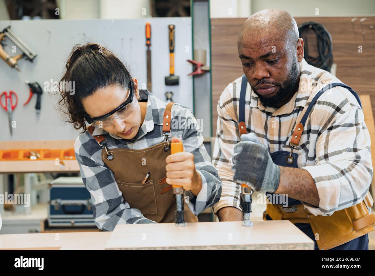 Eine starke Arbeiterin. teamarbeit beim baumeister. Schreiner in der Holzwerkstatt. zimmermannschaft hilft beim Möbelbau. Harte Arbeit, Holzbrett fixieren Stockfoto