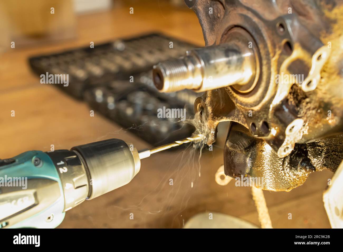 Beim Gewindedrehen entsteht Rauch im Lager der Hinterradnabe. Autoservice. Automechaniker arbeiten. Werkzeugkasten im Hintergrund. Gelbes Licht. Stockfoto