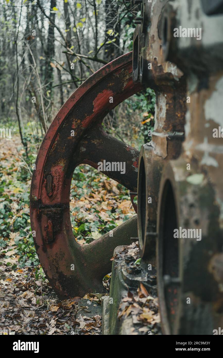 Detail des roten Rads eines alten verrosteten Luftkompressors im Wald. Industrielle Geschichtsmaschine. Eisen- und Stahlproduktion. Verlassene Maschine. Stockfoto