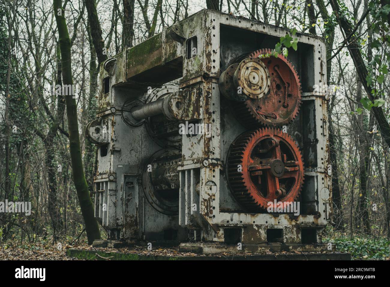 Eine alte verlassene Blechbearbeitungsmaschine im Wald. Eisen- und Stahlproduktion. Industrielle Geschichtsmaschine. Rote Zahnräder. Stockfoto