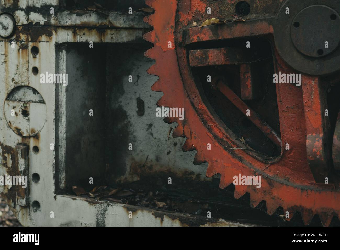 Detail des roten Zahnrads einer alten, stillgelegten Blechbearbeitungsmaschine im Wald. Eisen- und Stahlproduktion. Industrielle Geschichtsmaschine. Stockfoto