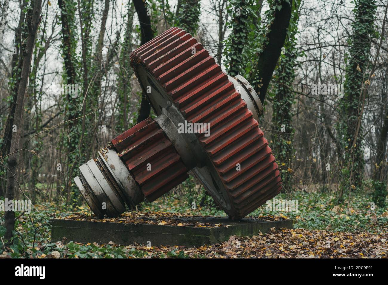 Seitenansicht eines alten roten Zahnrads im Wald. Industrielle Geschichtsmaschine. Verlassene Maschine. Eisen- und Stahlproduktion. Stockfoto