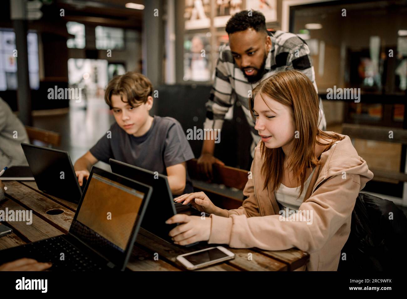 Teenager-Schülerin fragt männlichen Lehrer über Laptop, während er auf der Highschool auf einer Bank sitzt Stockfoto