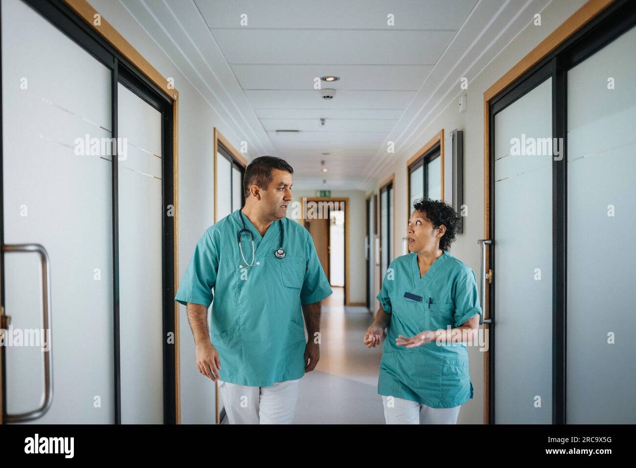 Multiethnische männliche und weibliche Gesundheitspersonal diskutieren während des Spaziergangs im Krankenhausflur Stockfoto