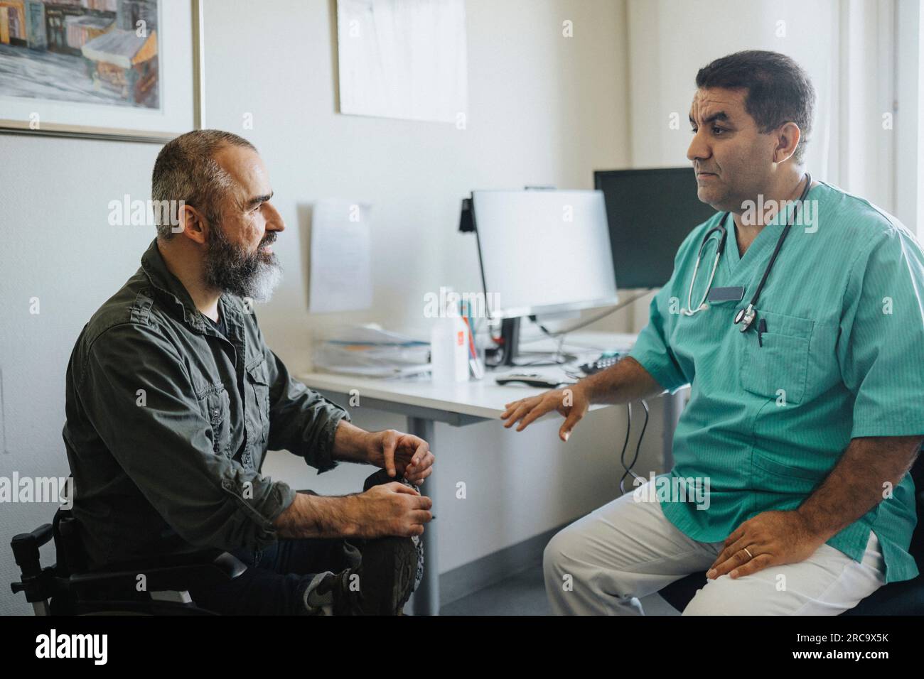 Reife Arztbesprechung mit Rollstuhlsitzendem Patienten im Krankenhaus Stockfoto