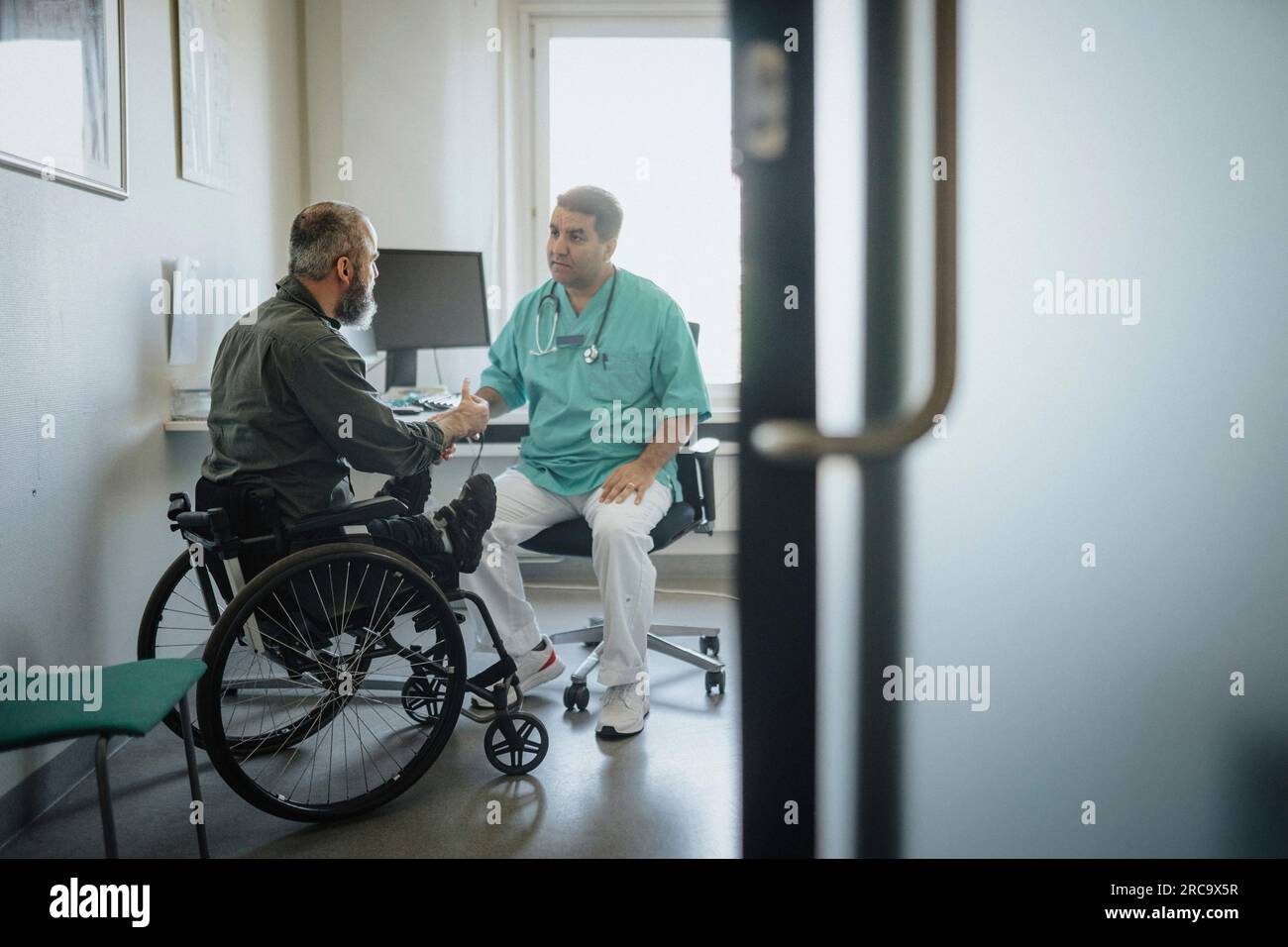 Arzt diskutiert mit männlichem Patienten im Rollstuhl im Krankenhaus Stockfoto